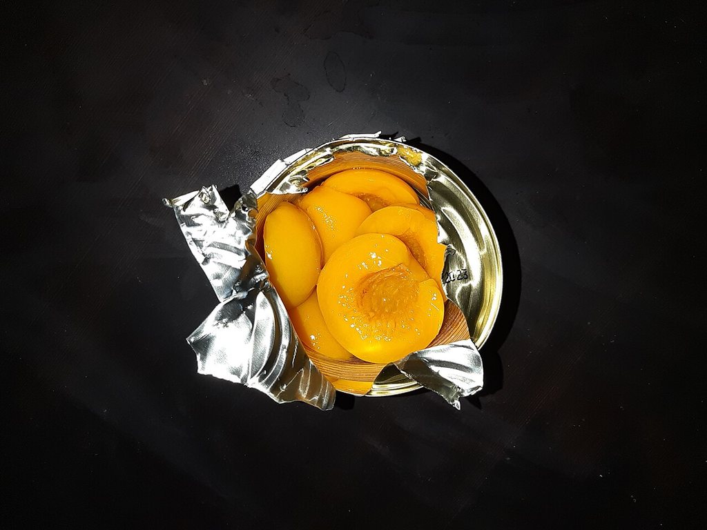 An opened can of peach halves, with a code stamped on the lid