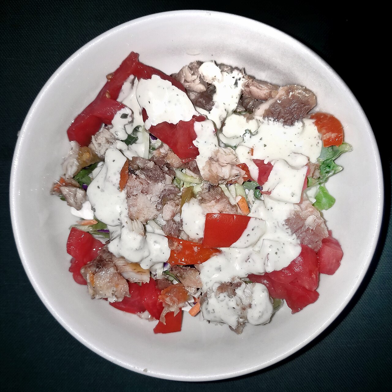 A salad topped with a creamy green dressing in a white bowl